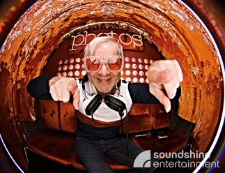 DJ.jpg DJ mit Glitzersonnenbrille und Kopfhörern um den Hals schaut in eine Fischaugenkamera
