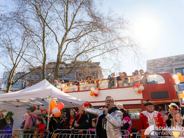 Karneval, Doppeldeckerbus,Rosenmontag.jpg Carnival event with costumed people outdoors and a presenter speaking into a microphone in the foreground