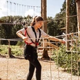 Kletterwald Surwold 1.jpg Person mit Klettergurt balanciert auf Seilen in einem Hochseilgarten zwischen Bäumen im Sonnenschein.