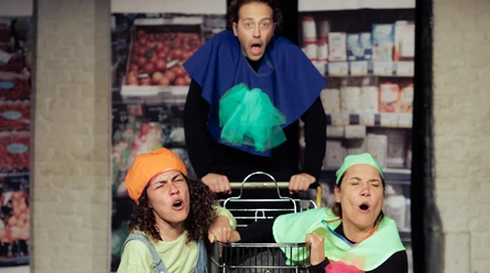 Horizont Theater Three people stand around a shopping cart with surprised expressions. They are wearing imaginative costumes.