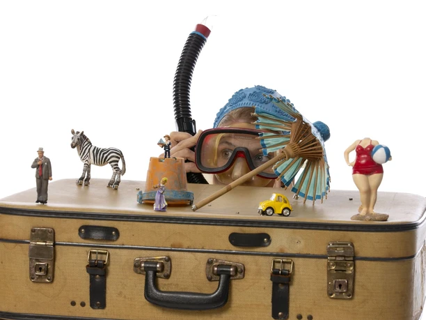 Taucher Figurentheater__MartinaBuchholz_WEB.jpg Frau mit Taucherbrille hinter Koffer, umgeben von Miniaturfiguren, Spielzeugauto und Papierschirm.