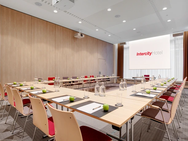 IntercityHotel Frankfurt Hauptbahnhof Süd - Raum 1 Heller Tagungsraum mit U-Bestuhlung, Tischen und Wandverkleidung in Holzoptik.