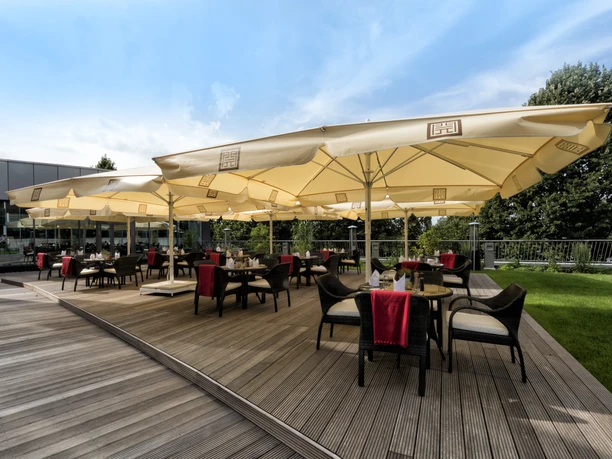 Delta Hotels by Marriott Frankfurt Offenbach - Terrasse Weitläufige Terrasse des Delta Hotels by Marriott Frankfurt Offenbach mit aufgespannten Sonnenschirmen unter blauem Himmel.
