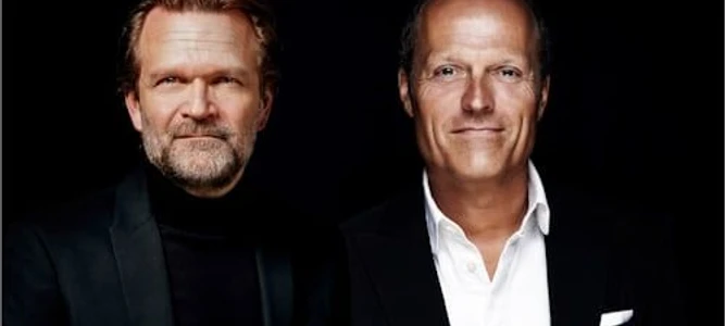 Zwei Männer in Anzug stehen nebeneinander und lächeln in die Kamera.