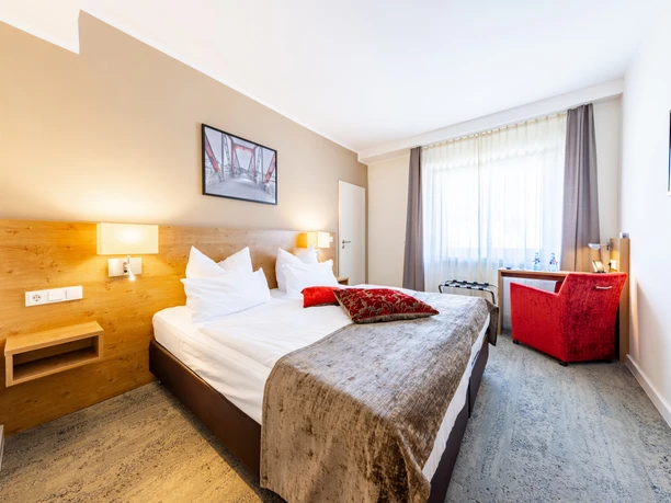 Maingau Hotel - Hotel rooms A bright hotel room with a double bed, red armchair and table.