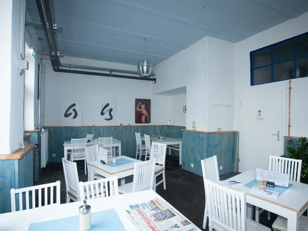 (c)Helmut_Gross__K5303.jpg Heller Gastraum mit weißen Holzmöbeln, blauen Wandpaneelen und moderner Kunst an den Wänden.