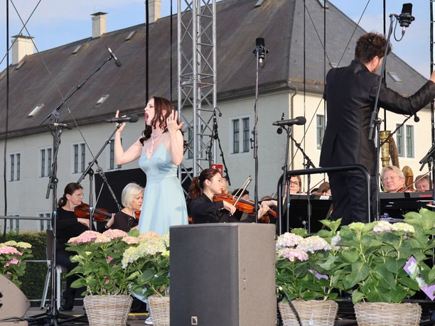 NWD Schloss Benkhausen Sängerin mit Orchester bei Open-Air-Auftritt vor hellem Schlossgebäude und Blumen