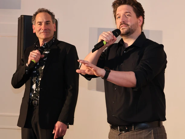 Ethan Freeman und Florian Hinxlage Zwei Männer auf einer Bühne mit Mikrofonen während eines Auftritts in ruhiger Pose