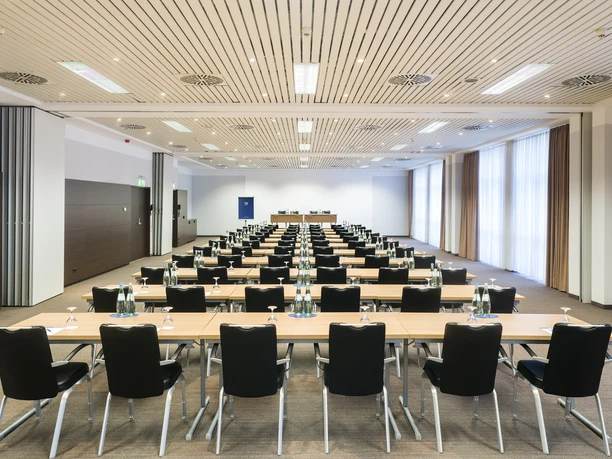 NH Frankfurt Airport West - Ein großer, heller Konferenzraum im NH Frankfurt Airport West, bestuhlt in Kinobestuhlung mit vielen Tischen und Stühlen für ein großes Event oder Seminar.