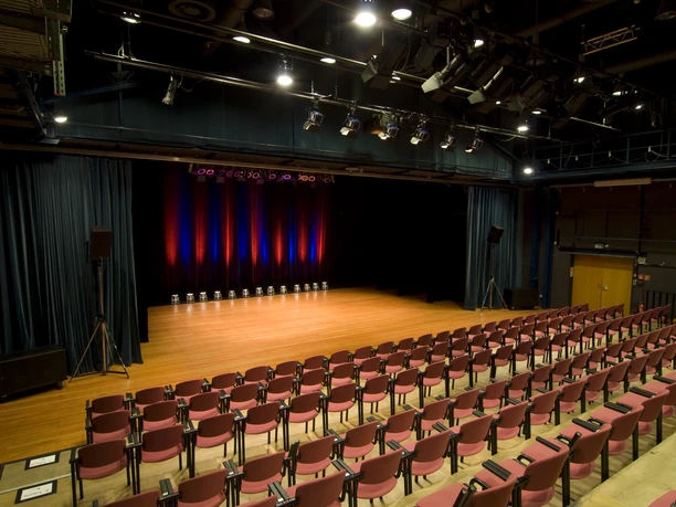 MICE 9075_002 (c) Rillke und Sandelmann Fotografie.jpg Blick in einen modernen Theatersaal mit leerem Parkett, roten Stühlen und beleuchteter Bühne