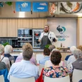 © Björn Hake.jpg Koch erklärt vor Publikum die Zubereitung von Fischgerichten in moderner Studioküche in Bremerhaven.