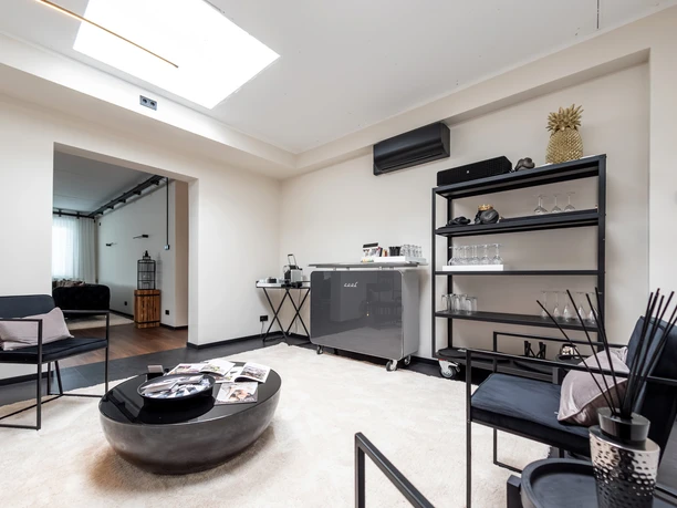 LOFT By CKE - Bar Ein heller Raum mit kleiner Bar, schwarzem Regal, Stühlen und zentralem Couchtisch.