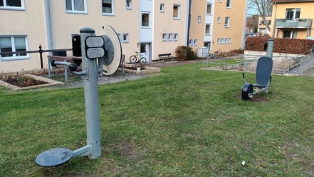 Fitnessgeräte_Eichendorffplatz_Salzgitter-Bad (7)_HD_16zu9.jpg Zwei Outdoor-Fitnessgeräte auf einer Rasenfläche vor mehrstöckigen Wohnhäusern in Salzgitter-Bad.