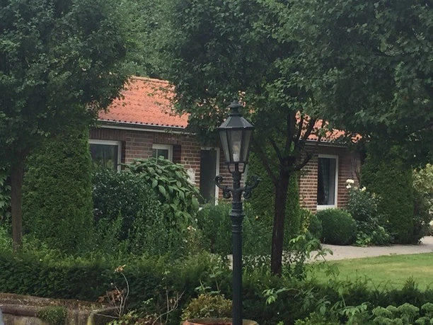 speicherbecken ferienhaus.jpg Backsteinhaus mit rotem Ziegeldach, umgeben von grünen Sträuchern, Bäumen und Gartenlaterne.