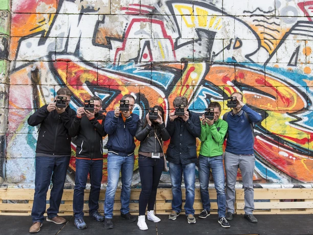 ctc events - Graffiti-Tour Eine Gruppe von sieben Personen steht vor einer bunten Graffiti-Wand. Alle halten eine Kamera vor ihr Gesicht, um die Wand zu fotografieren.