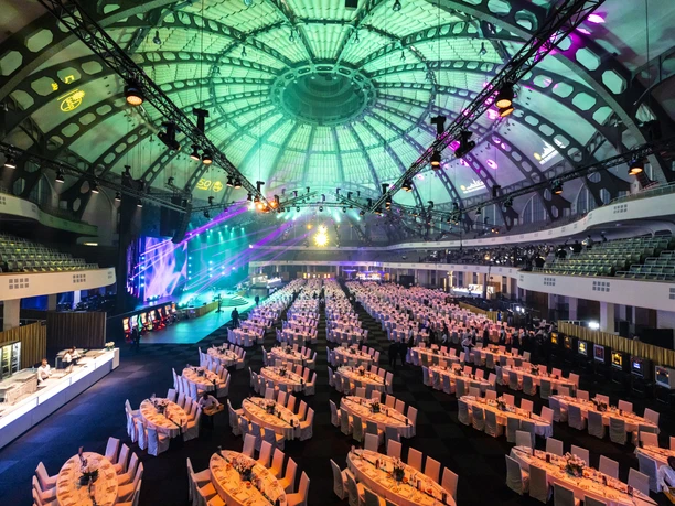 ctc events - Galaabend Festhalle Eine große Festhalle mit vielen weiß gedeckten Tischen für eine Gala. Die Kuppeldecke ist grün und lila beleuchtet.