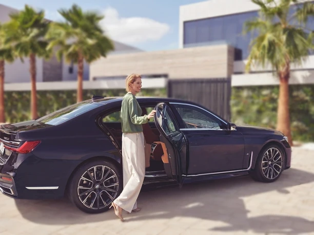 SL-Limousinen I Chauffeur & Limousinenservice - modernen Villa zeigt eine Dame, die in ein Auto einsteigt, vor einer modernen Villa mit Palmen.