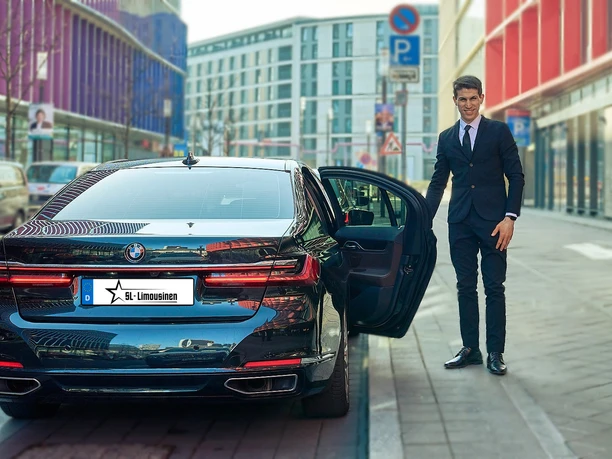 SL-Limousines I Chauffeur & Limousine Service - BMW Luxury Limousine An elegantly dressed chauffeur stands next to a black BMW luxury sedan with an open door.