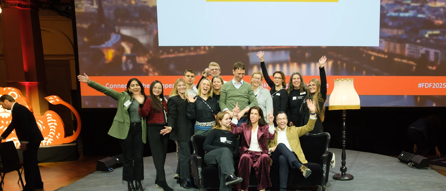 MIT Event- & Incentive-Management GmbH - large group of people A large group of people pose laughing on a stage in front of a screen with the words "FRANKFURT DIGITAL FINANCE & European Fintech Day".