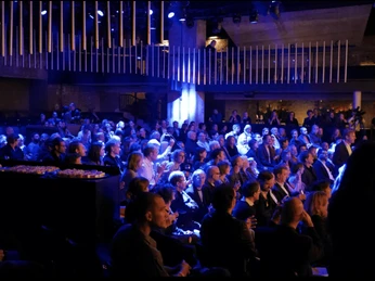Location Rhein-Main - Event room Dark event room with many spectators in blue light following a performance or presentation.