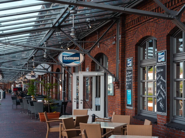 Abelmann IMG_6451 (c) Nastasia Simms_Erlebnis Bremerhaven_CC BY_NENNUNG DES COPYRIGHTS.JPG Überdachte Außenterrasse des Bistros Abelmann an roter Backsteinfassade mit Sitzplätzen am Hafen