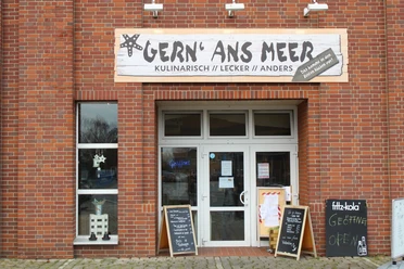 Backsteinfassade mit Eingang des Fischimbisses Gern’ Ans Meer und Tafeln mit Speisenangebot.