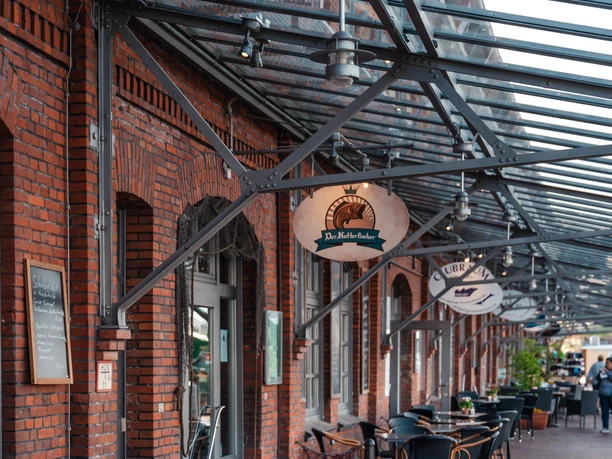 Kutterfischer IMG_6449 (c) Nastasia Simms_Erlebnis Bremerhaven_CC BY_NENNUNG DES COPYRIGHTS.JPG Außenterrasse des Restaurants Der Kutterfischer in Bremerhaven mit Tischen unter Glasdach.