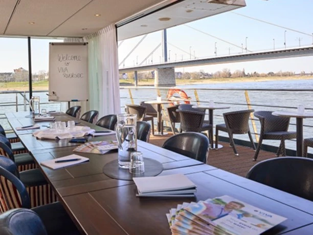 VIVA RIVERSIDE Altstadt - Bistro Restaurant mit Innen- und Außensitzplätzen, mit Blick auf den Fluss und die Brücke.