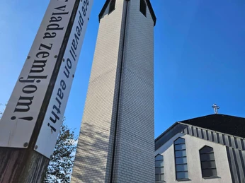 Weißer Kirchturm neben Friedenspfahl vor blauem Himmel neben dem hellen Kirchengebäude
