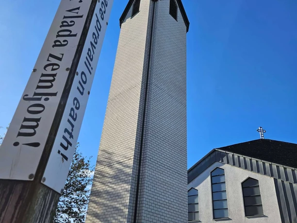 Langeland Nepomuk-Kirche Weißer Kirchturm neben Friedenspfahl vor blauem Himmel neben dem hellen Kirchengebäude