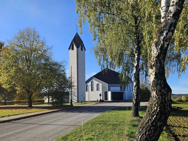 Langeland Nepomuk-Kirche Weißer Kirchturm und Kirchenbau zwischen Bäumen an einer ruhigen Straße bei klarem Himmel.
