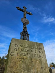 Langeland Schwarzes Kreuz Steinkreuz mit Metallkruzifix und gut lesbarer Widmung vor klarem blauen Himmel.