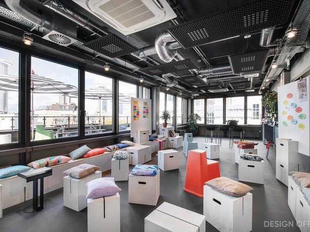 Design Offices Frankfurt Wiesenhüttenplatz - Worklab Heller Workshop-Raum mit bunten Kissen, Boxhockern und City-Ausblick.