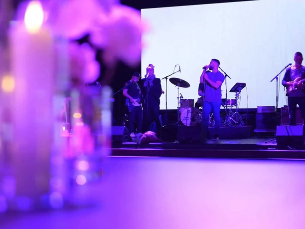 formwandler events - Band Eine Live-Band tritt auf einer Bühne auf, im Vordergrund unscharfe Kerzen und Blumen, alles in violettes Licht getaucht.