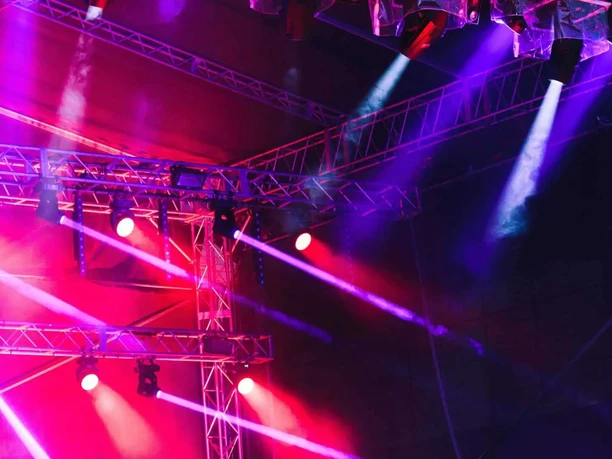 formwandler events - Stage lights Complex scaffolding with numerous stage lights that project intense red and violet beams into the darkness.