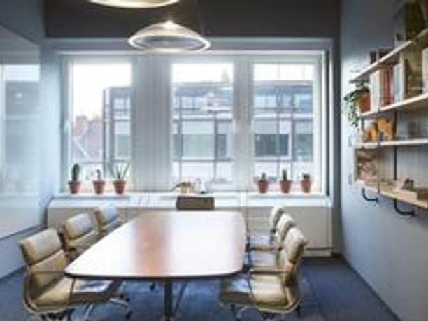 Design Offices Frankfurt Westendcarree - Besprechungsraum heller Besprechungsraum mit Holztisch, Ledersesseln, Fensterblick und einem Bücherregal.