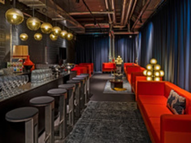Design Offices Frankfurt Westendcarree - Bar Dunkle, moderne Bar mit langer Theke und leuchtend orangen Lounge-Sofas.