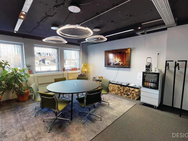 Design Offices Frankfurt Barckhausstraße - Moderner Besprechungsraum Moderner Besprechungsraum mit rundem Tisch, schwarzen Decken und großen Pflanzen. Ein Bildschirm zeigt ein Feuer an.