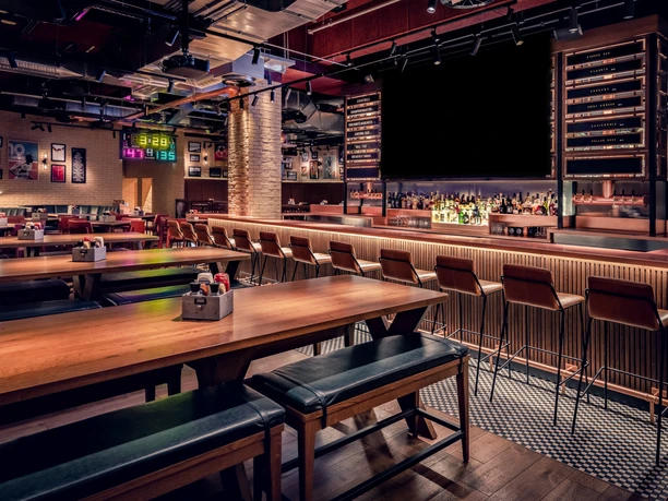 Frankfurt Marriott Hotel - Champions Sportsbar Die Champions Sportsbar mit einer langen Bar, Holztischen und Bänken. Die Atmosphäre ist durch die Beleuchtung warm und gemütlich.