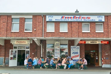 Menschen sitzen vor einem Backsteinhaus in Bremerhaven und essen an Tischen eines Fischimbisses.
