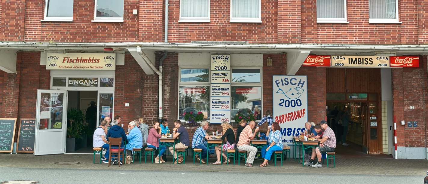 Stadtansichten von Bremerhaven Menschen sitzen vor einem Backsteinhaus in Bremerhaven und essen an Tischen eines Fischimbisses.
