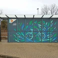 Fahrradboxen mit blau-grünem Blättermotiv und überdachtem Bereich an einem Bahnhof.