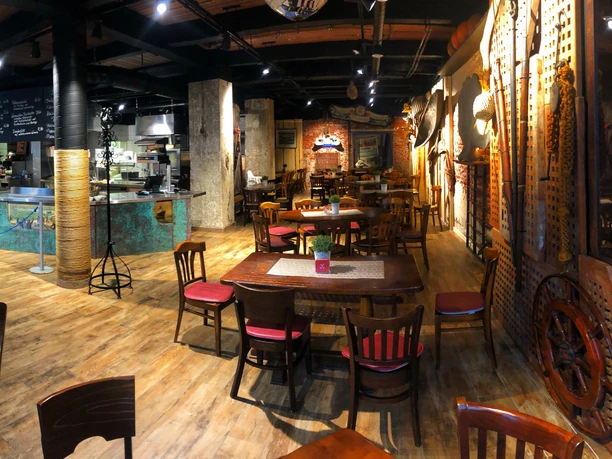 Kombüse IMG_2604.jpeg Maritim gestaltetes Fischbistro mit Holzmöbeln, Schiffsdekor und Blick auf die offene Küche.