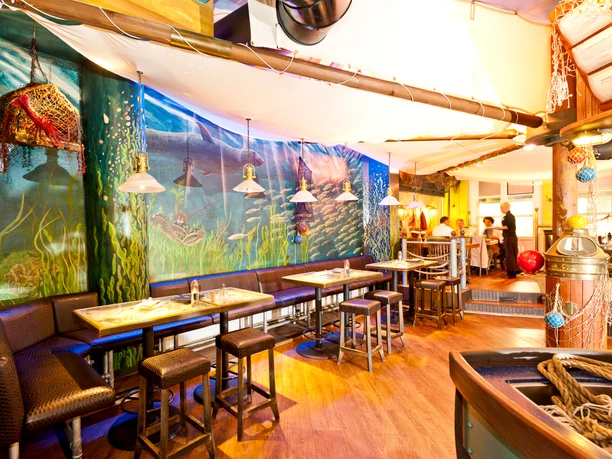 8-Fiedlers Kutterfischer_0321.jpg Maritim gestalteter Gastraum mit Wandmalerei, Holzmöbeln und Beleuchtung im Stil eines Fischkutters.