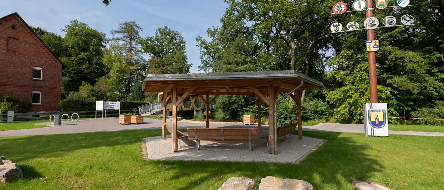 Holzpavilion mit Sitzbänken, daneben ein Maibaum, Rastplatz direkt am Heubach