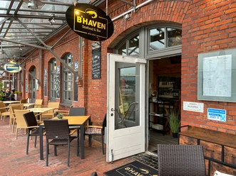 Eingang der B’HAVEN Seafood & Bar mit überdachter Außenterrasse und roten Backsteinfassaden.