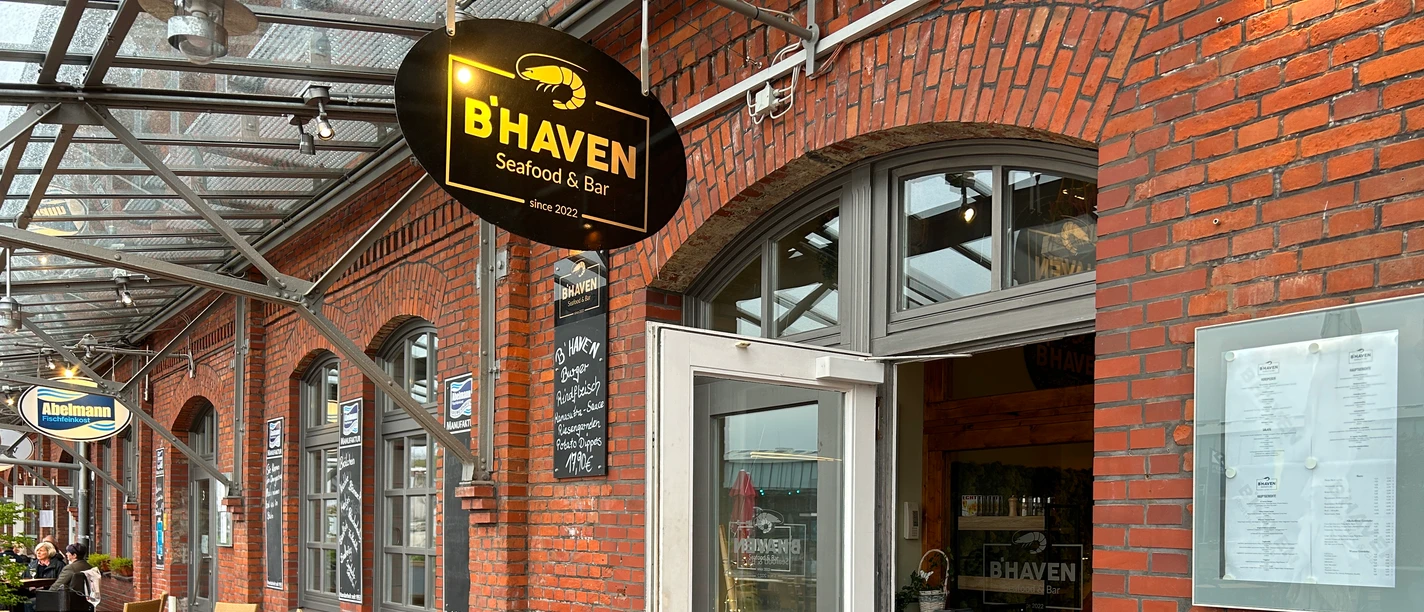 IMG_3008 (c) Tanja Mehl_Erlebnis Bremerhaven.JPG Eingang der B’HAVEN Seafood & Bar mit überdachter Außenterrasse und roten Backsteinfassaden.