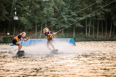 Wakeborden in bei Wasserski Langenfeld Zwei lachende Wakeboarderinnen gleiten über das Wasser bei Wasserski Langenfeld, spritzende Wellen.