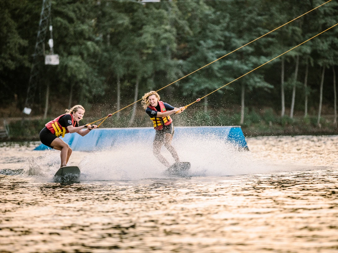 Wakeborden in bei Wasserski Langenfeld Zwei lachende Wakeboarderinnen gleiten über das Wasser bei Wasserski Langenfeld, spritzende Wellen.
