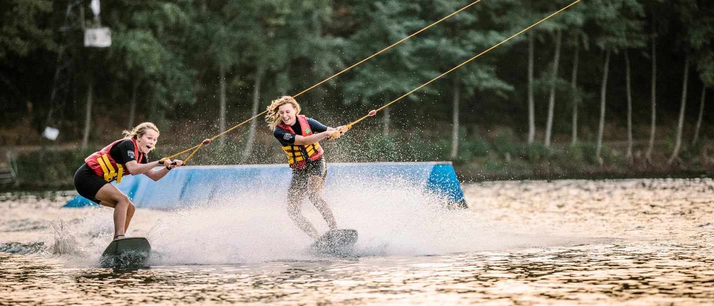Wakeborden in bei Wasserski Langenfeld Zwei lachende Wakeboarderinnen gleiten über das Wasser bei Wasserski Langenfeld, spritzende Wellen.